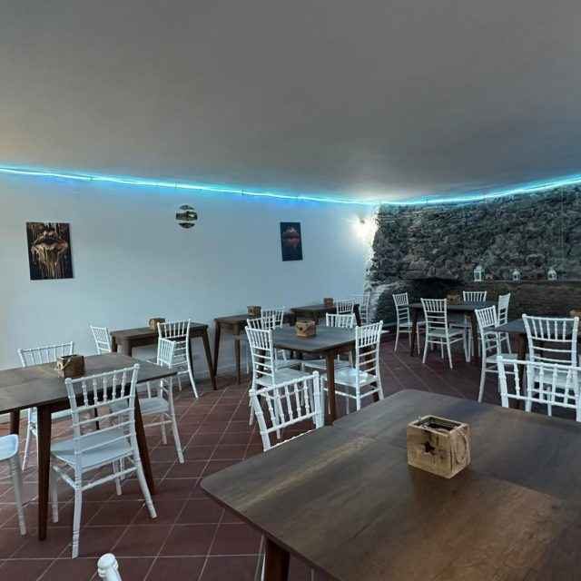 Modern restaurant interior with wooden tables and white chairs, softly lit with blue lights.